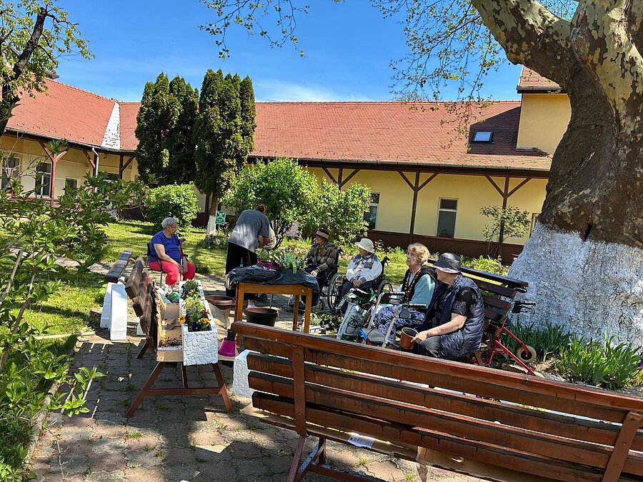 Der Hof mit Bänken und Platane, im Hintergrund Bewohner beim Pflanzen