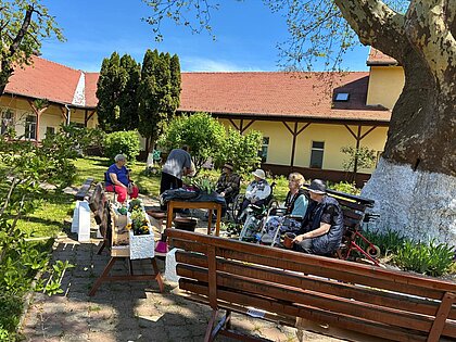 Der Hof im Mai: Bänke unter der Platane, frisch gesetzte Blumen, Bewohner im Schatten