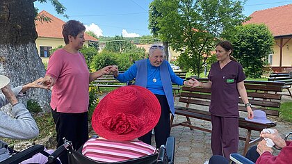 Eine Mitarbeiterin und eine Besucherin tanzen mit einer Bewohnerin im Hof