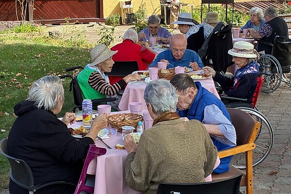 Bewohnerinnen und Bewohner beim Essen im Schatten