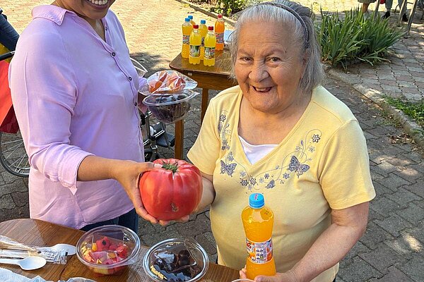 Eine Mitarbeiterin reicht einer Bewohnerin eine große Tomate