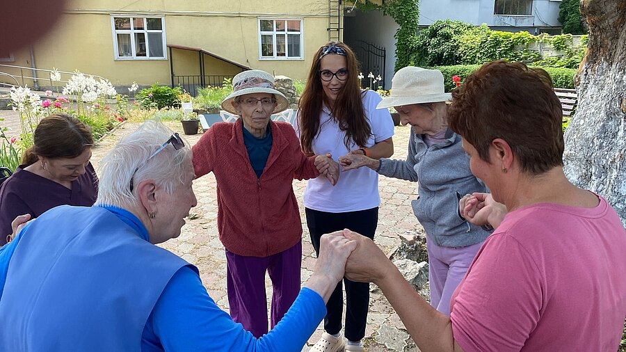 Bewohnerinnen, Besucherinnen und Team tanzen Hand in Hand im Hof