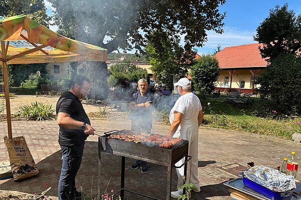 Zwei Männer am rauchenden Grill im Hof