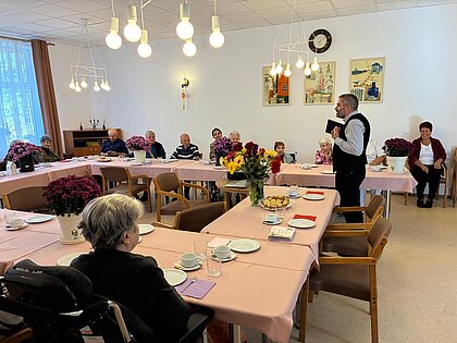 Festlich gedeckte Tische mit Chrysanthemen im Speisesaal, ein Redner spricht zu den Bewohnern