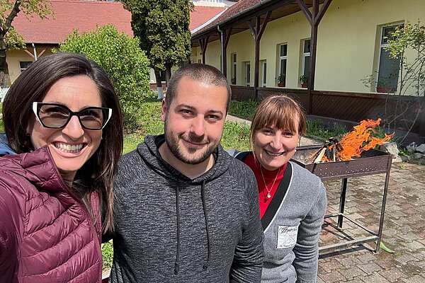 Drei Mitarbeiterinnen und Mitarbeiter vor dem Grill im Hof
